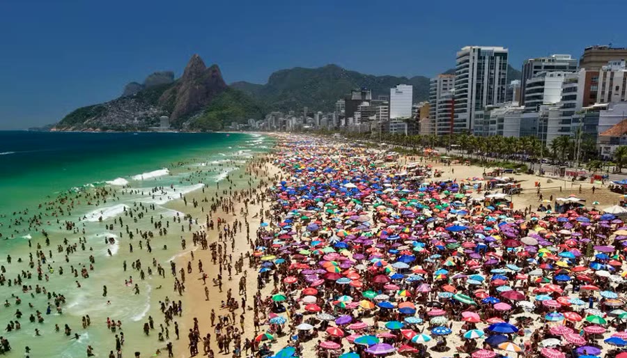 Aerial view of Ipanema beach covered in colorful umbrellas, with the mountains behind